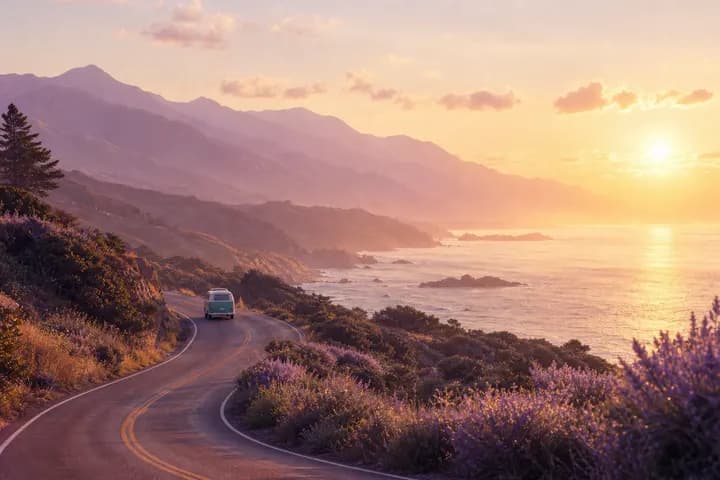 A coastal road winding toward lavender mountains and a sunrise sea.
